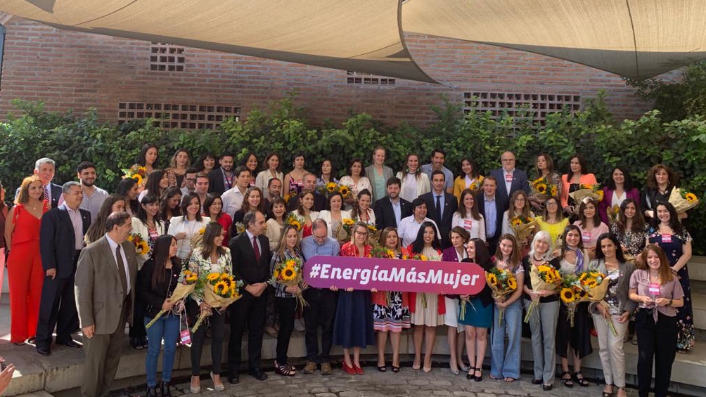 three rows of women stand in front of 'Energía mas Mujer' banner