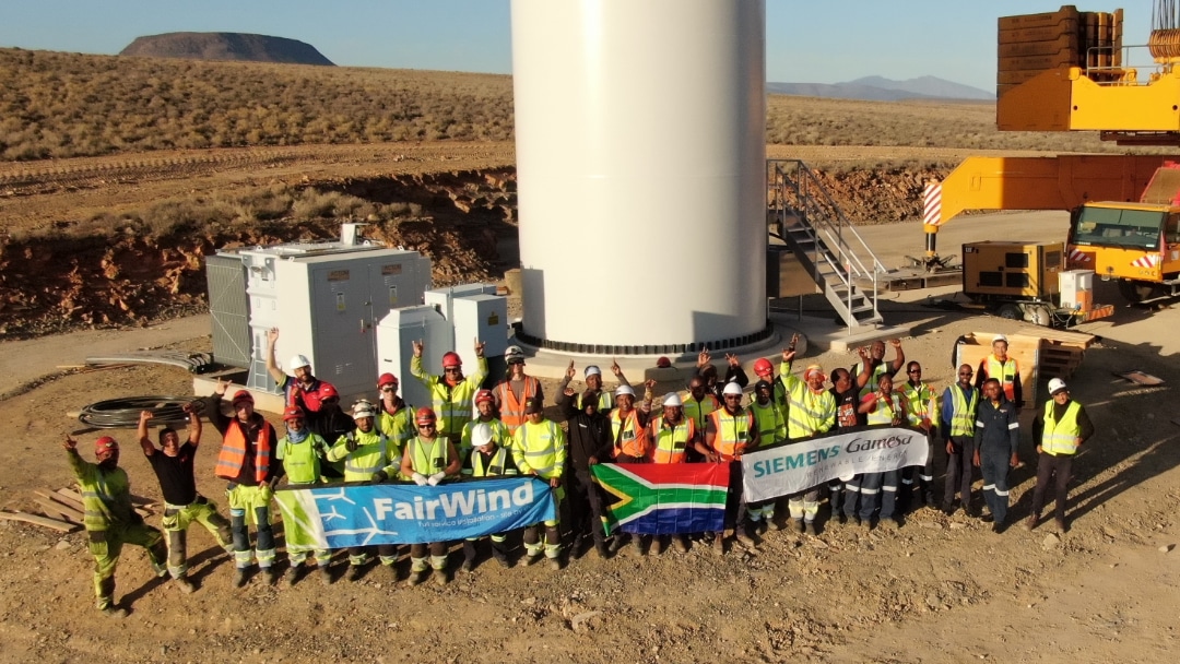 Aerial picture of construction workers holding contractor and South Africa flags in front of erected turbine base