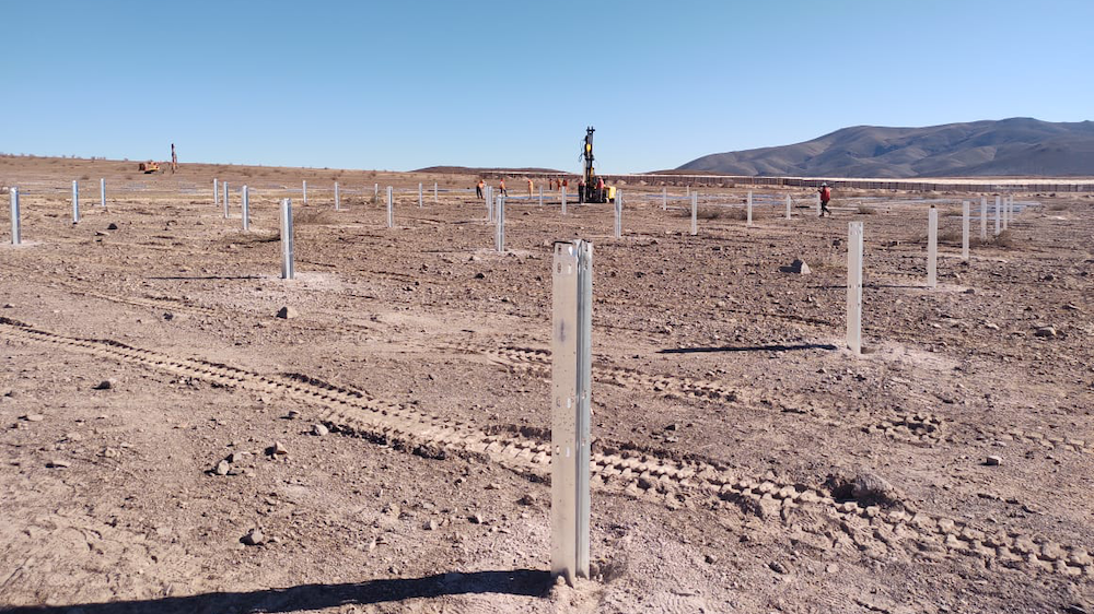 Picture of brown dirt ground with solar poles in the ground and blue sky.