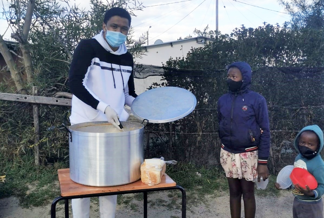 community helper serves soup from street canteen to two children