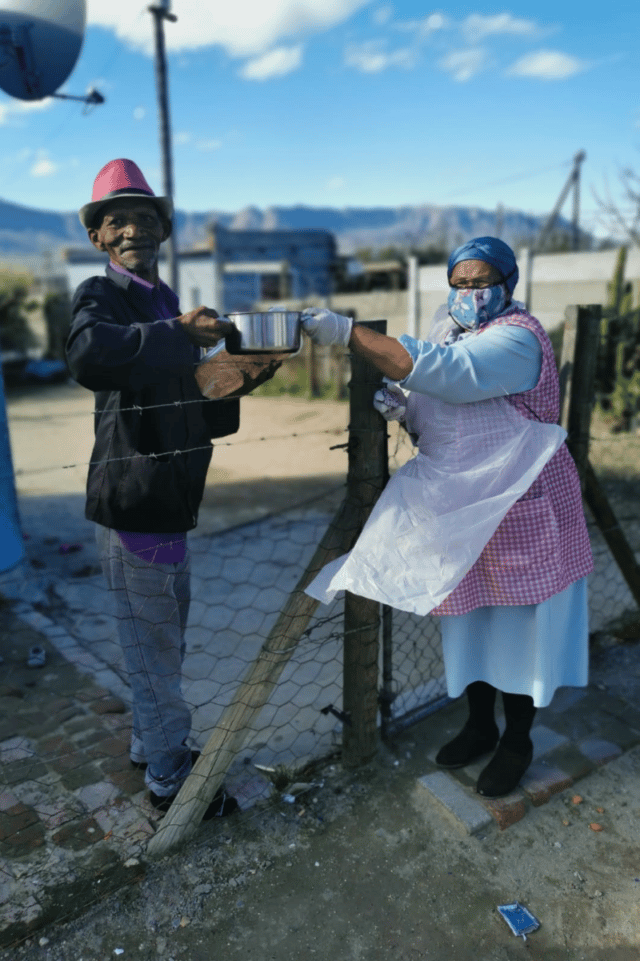 A volunteer hands over metal dish to elderly man