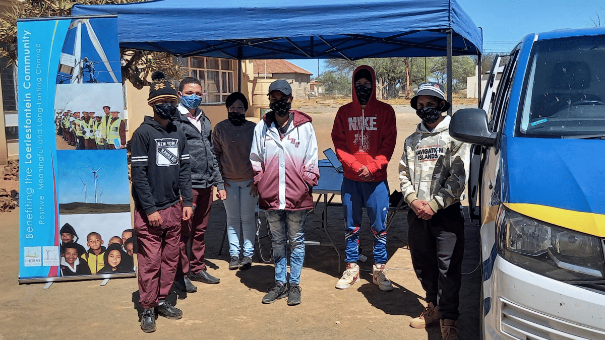 Group of school pupils wait in shade by community support van