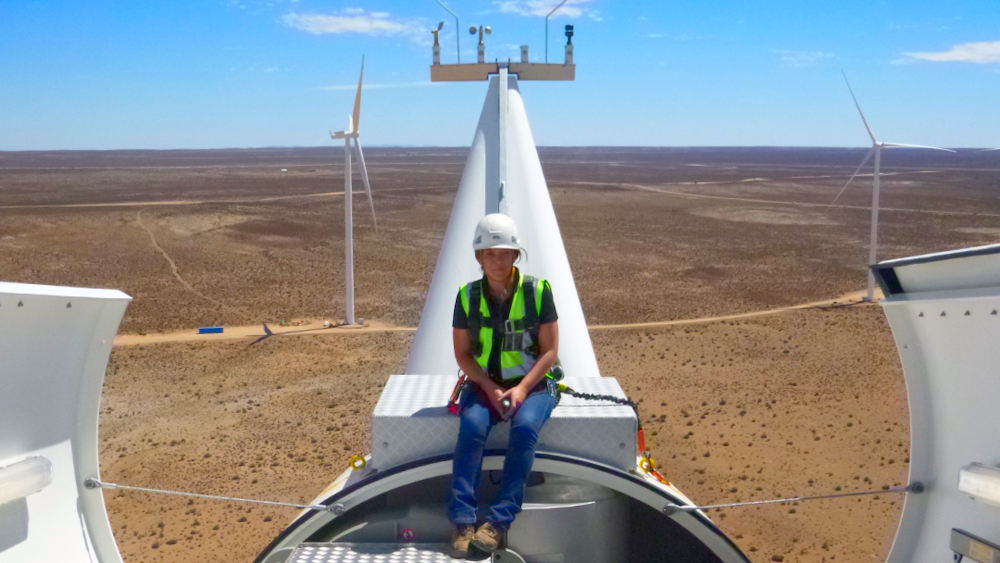 Leona Smith sitting on the top of a wind Turbine with a hard hat on and a high vis