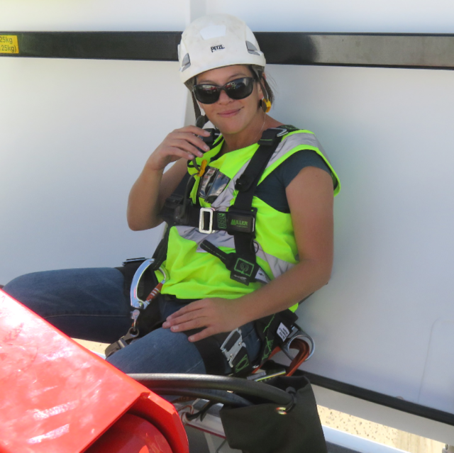 A pciture of a woman with a hard hat on, a high vis and a harness