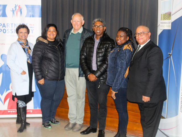 A line of 6 people, 3 men and 3 women standing smiling having their picture taken.