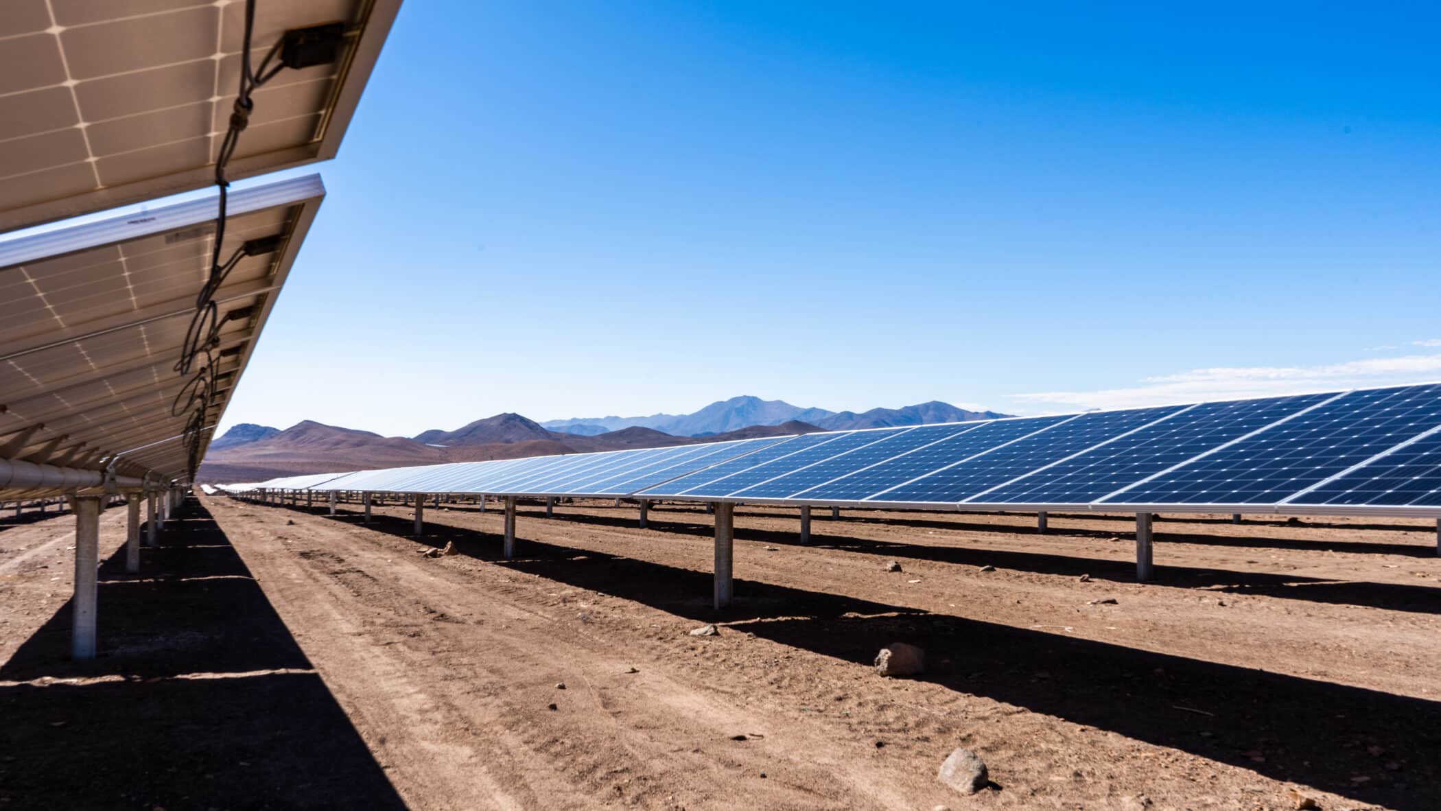 Low down shot beneath a row of solar pv panels in a solar farm with mountains in the distance
