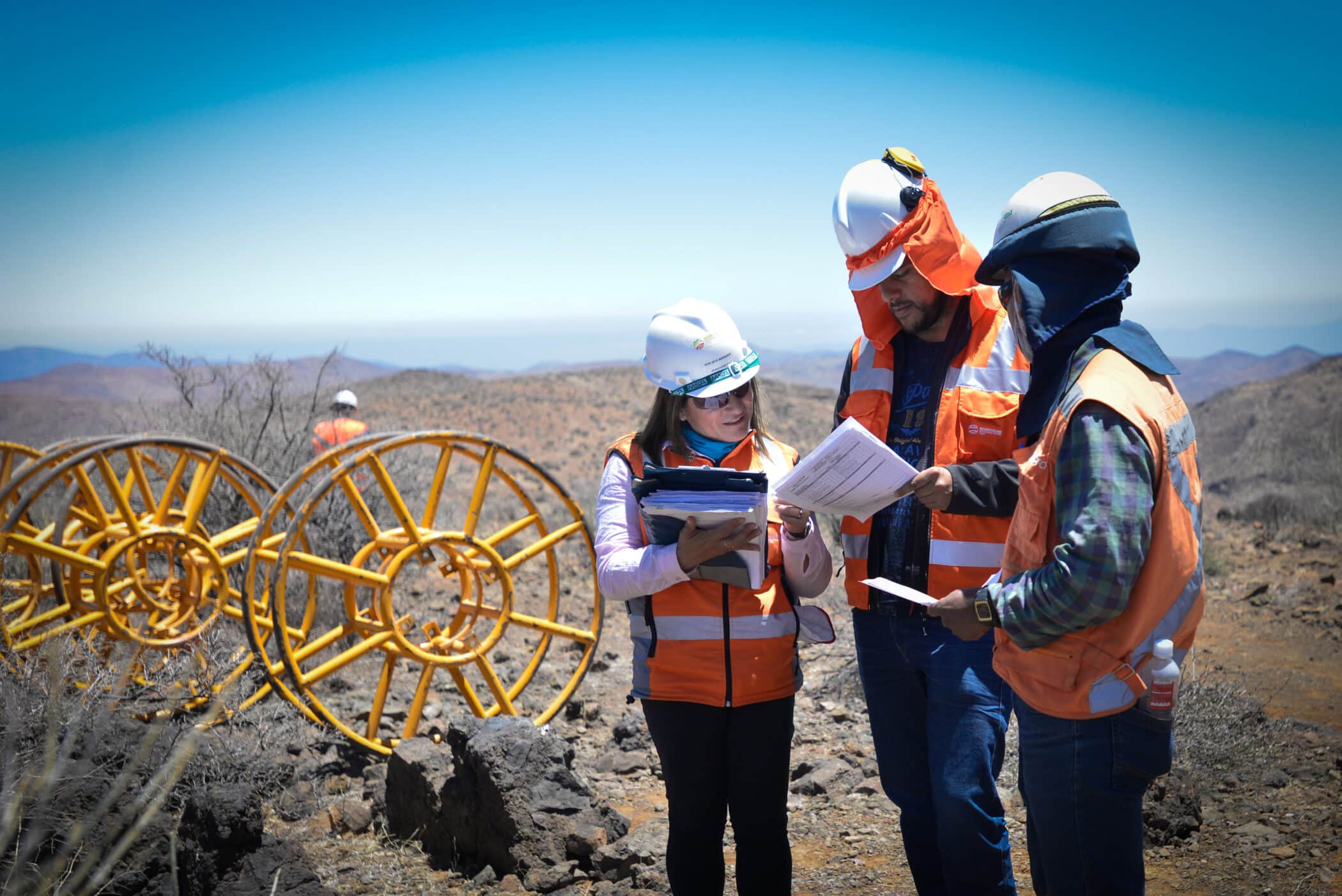 Three onsite team members in hi vis and protective equipment reviewing planning documents for renewable energy site - Mainstream renewable power - what we do