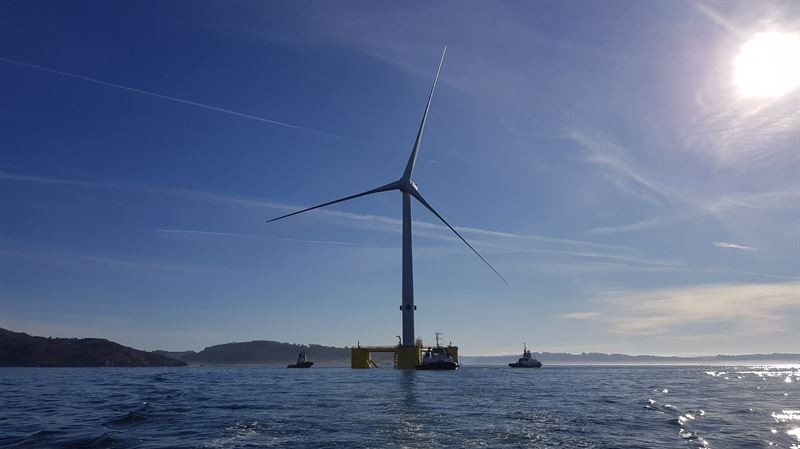 Floating offshore wind turbine with 3 sea vessels at base of turbine
